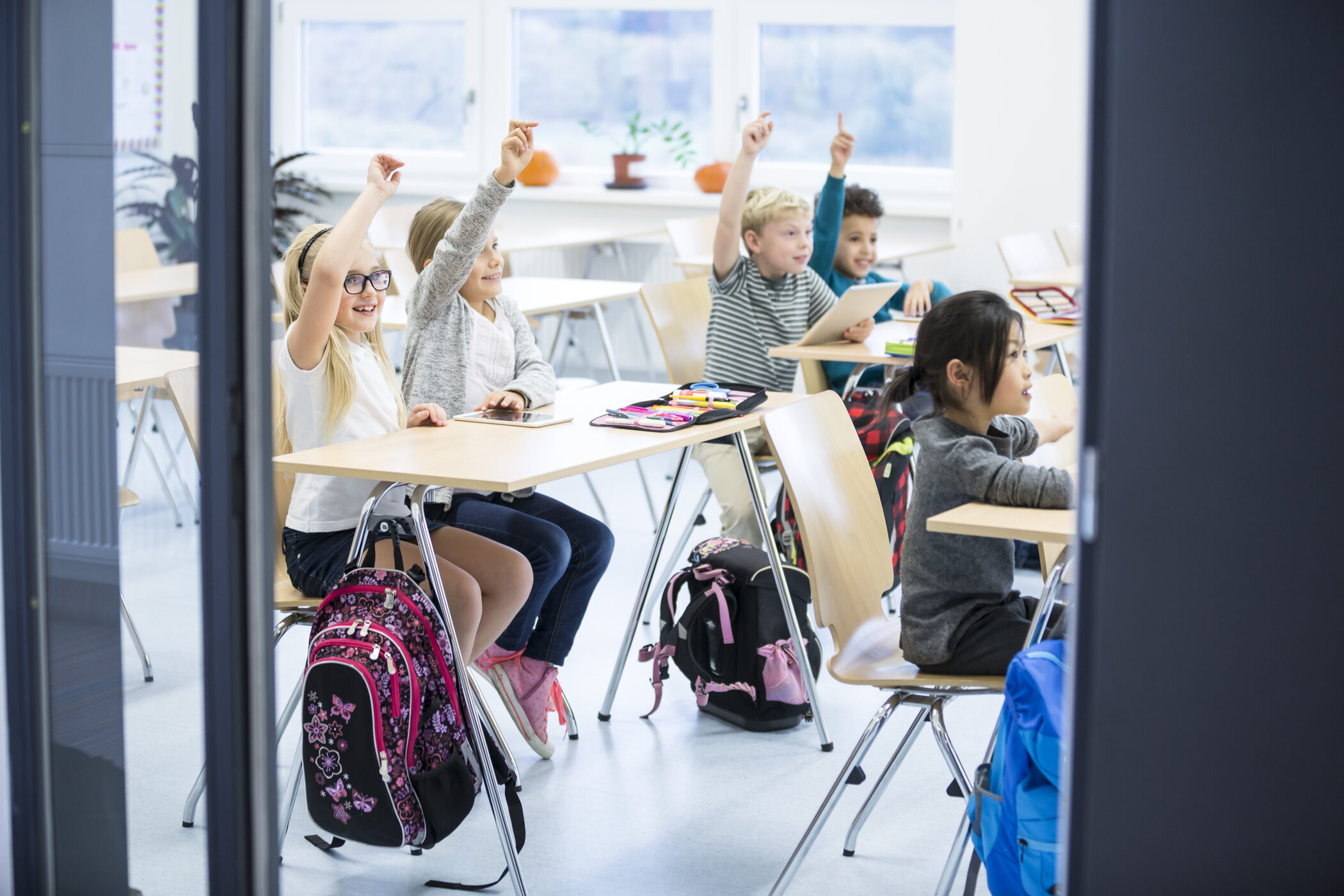 Children raising their hands in a bright classroom